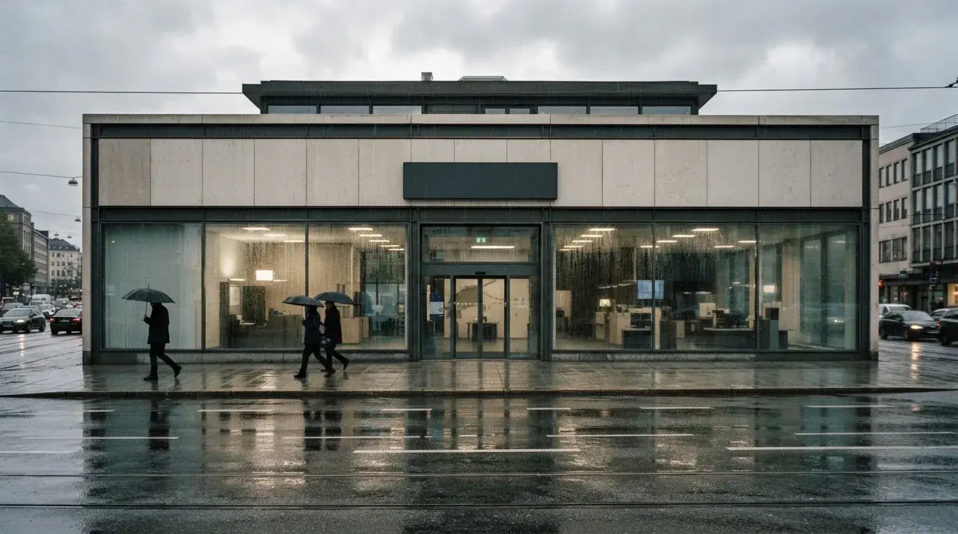 Bankfilial med store vinduer i en norsk by i regnvær, noen med paraplyer utenfor